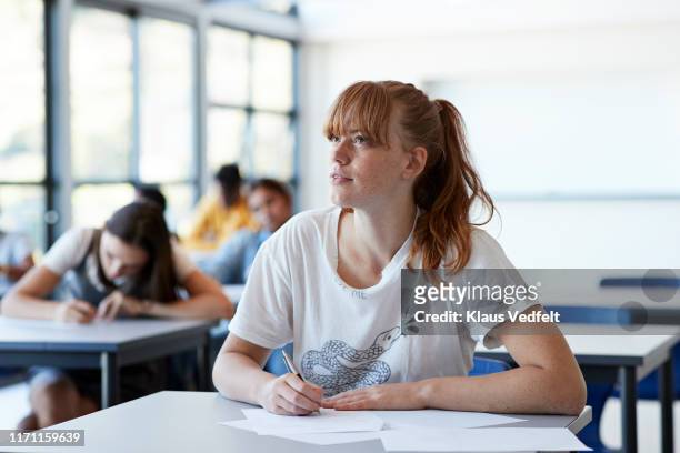 thoughtful student looking away while writing exam - school exam imagens e fotografias de stock