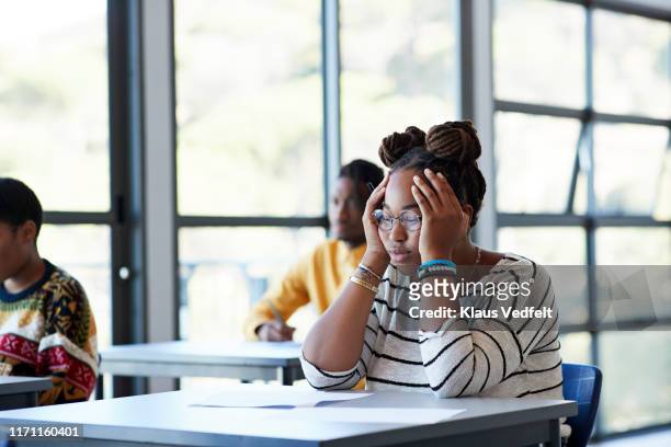 worried student sitting with head in hands at desk - exam photos et images de collection