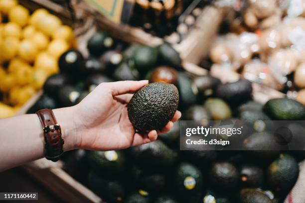 woman shopping for fresh fruit and vegetables in supermarket, close up of her hand choosing avocados - food decisions stock pictures, royalty-free photos & images