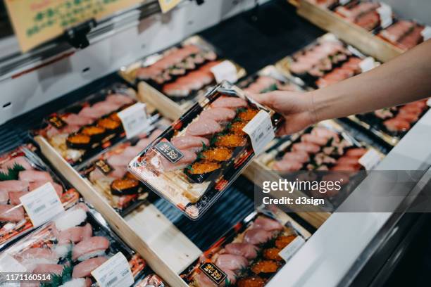 woman's hand choosing a box of fresh packaged sushi from the display fridge in the supermarket - viswinkel stockfoto's en -beelden