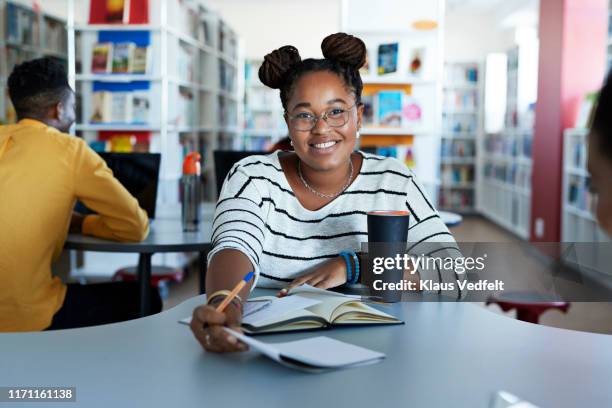 smiling female student studying at desk in library - differential focus education reach stockfoto's en -beelden