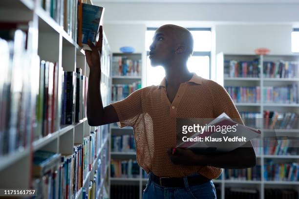 young man removing book from shelf in library - shelf strip stock pictures, royalty-free photos & images