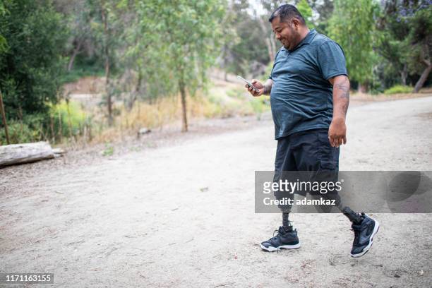 hispanic male amputee walking with smartphone - fat legs stock pictures, royalty-free photos & images