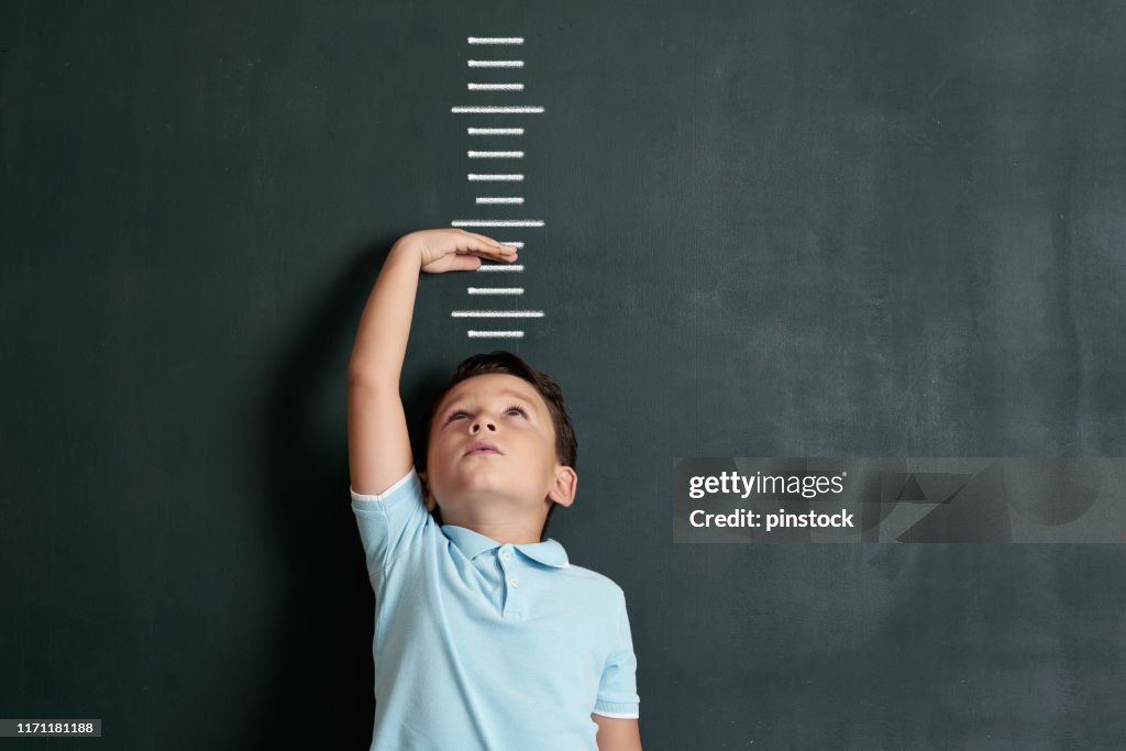 Niño midiendo su altura en la pared. Está creciendo tan rápido.