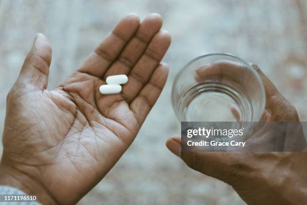 close-up view of hands holding pills and water - acetaminophen stock-fotos und bilder