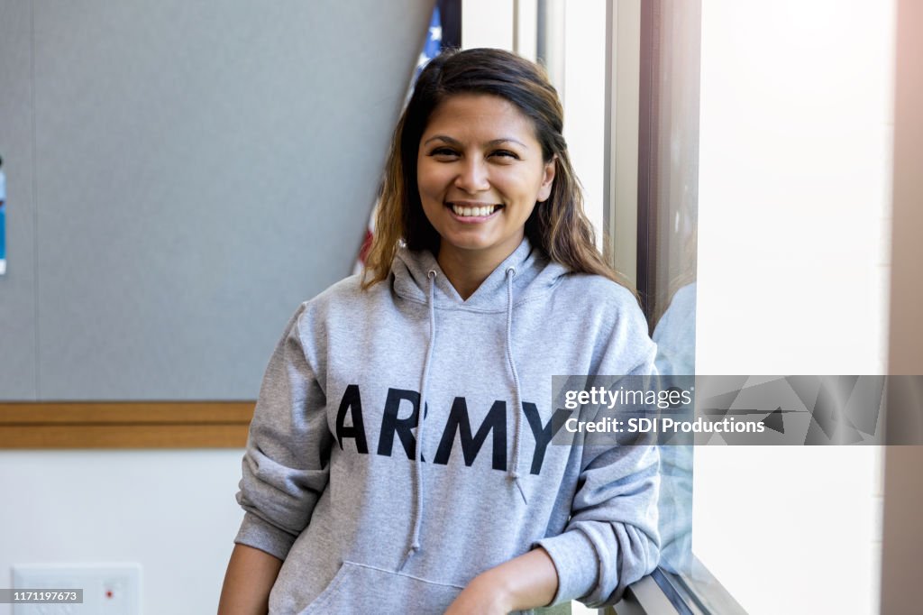 Female army vet leans against window and smiles for camera