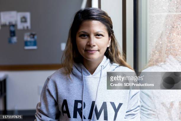attractive mid adult female army vet stands in sunlit window - army shirt stock pictures, royalty-free photos & images