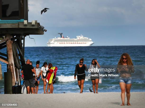 People walk on the beach at the Cocoa Beach Pier while a cruise ship leaves Port Canaveral ahead of the approaching Hurricane Dorian, on August 30,...