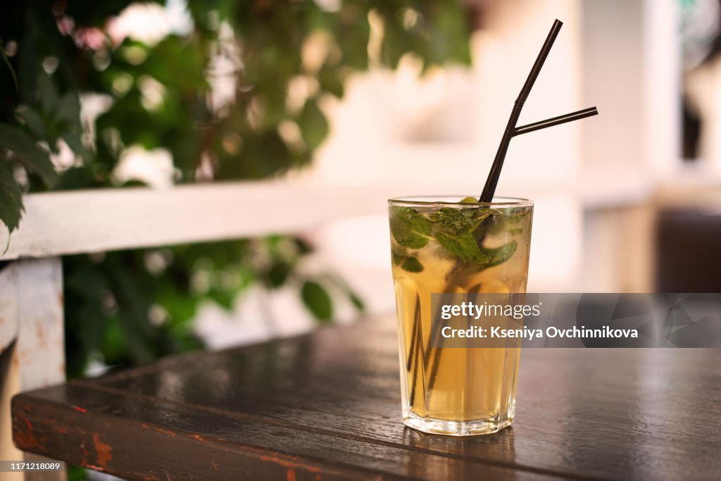 Low angle close up of ice cold modern gourmet craft cocktail of gin and tonic soda garnished by lemon slice and rosemary sprig sprinkled by juniper berries on bar with blurry restaurant bar background