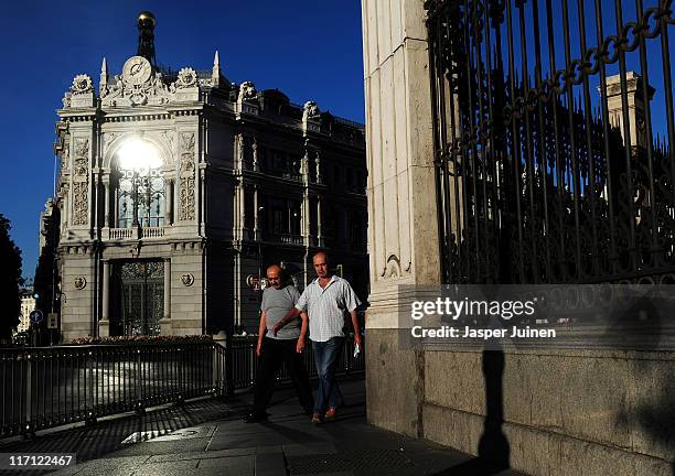 Pedestrians stroll past the national central Bank of Spain lit by the early morning sun on June 23, 2011 in Madrid, Spain. Eurozone finance ministers...