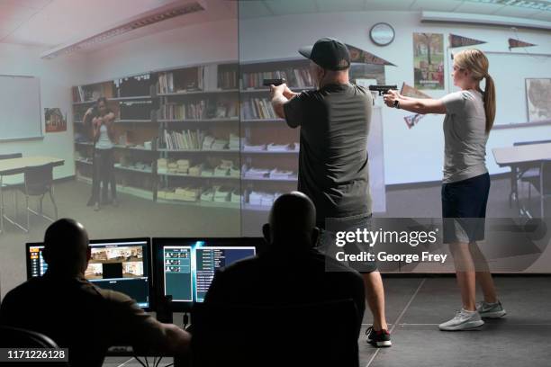 Utah teachers Anthony Bowder and Holli Averett interact with a video simulator that creates an active shooter scenario in a school during a training...