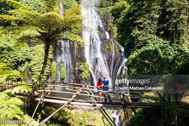 tourist couple looking at waterfall, munduk, bali, indonesia - bali waterfall stock pictures, royalty-free photos & images