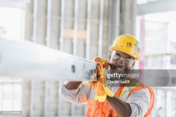 operaio edile afroamericano che trasporta travi metalliche - abbigliamento da lavoro foto e immagini stock
