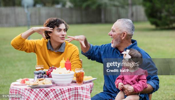 hispanischer vater, teenager-sohn und baby essen im freien - baby spielt mit essen stock-fotos und bilder