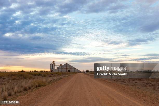 country road with grain silo in the distance - queensland farm stock pictures, royalty-free photos & images