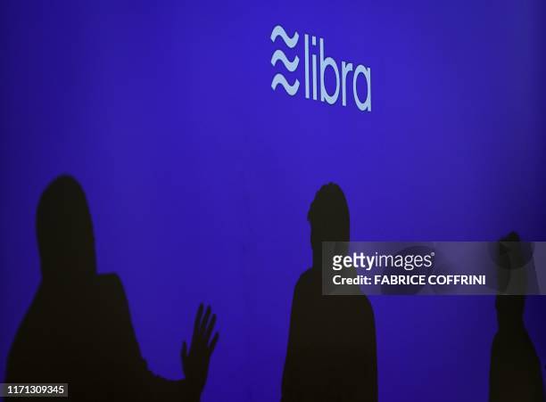 Silhouettes are seen beneath a sign of Libra, the cryptocurrency project launched by Facebook during a conference at marketing and communication...