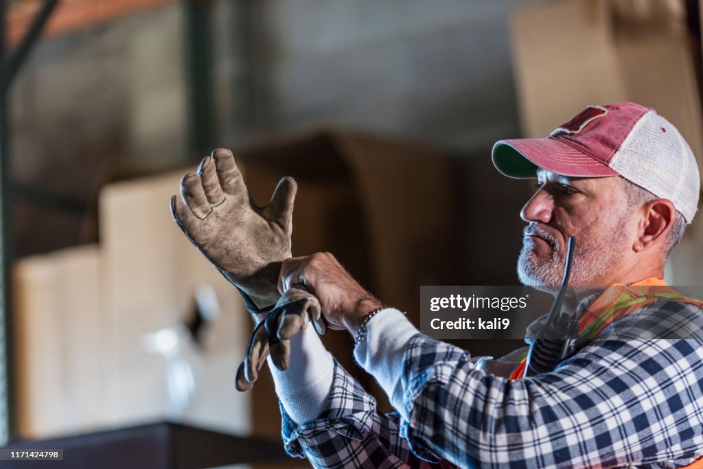 Hispanic man standing in warehouse donning work gloves