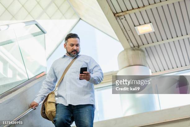 hispanic man walking, looking at mobile phone - chubby men stock pictures, royalty-free photos & images