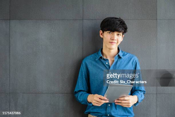 portret van jonge lachende aziatische business man holding digitale tablet computer op grijze achtergrond, kijken naar camera - handsome asian guy stockfoto's en -beelden