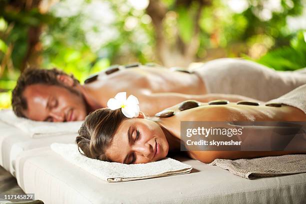 relaxed couple with eyes closed receiving hot stone therapy - massage therapy stock pictures, royalty-free photos & images