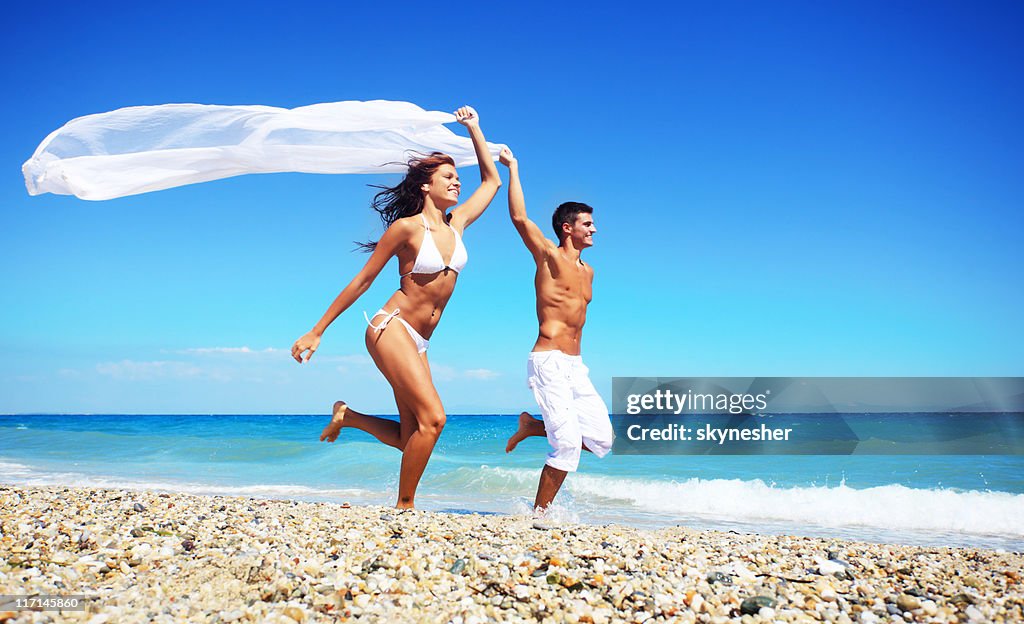 Paar läuft mit weißem Tüll am Strand.
