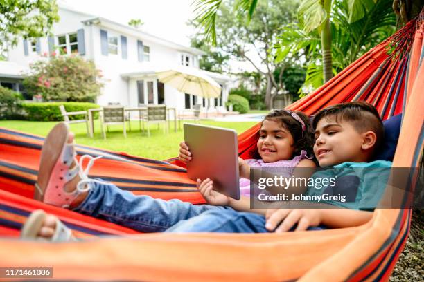 young hispanic siblings using digital tablet in hammock - miami house stock pictures, royalty-free photos & images