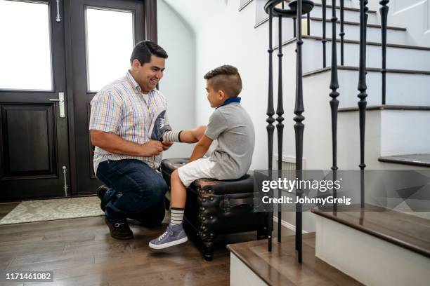 latin american father helping young son put on shoes - family smiling at front door stock pictures, royalty-free photos & images