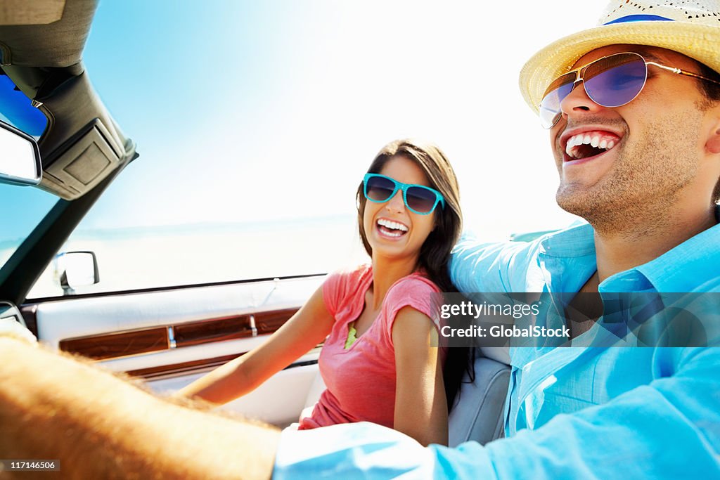 Cheerful young couple in a convertible car going for vacation