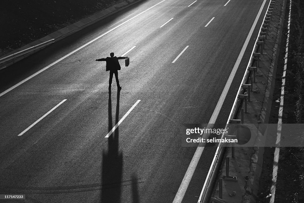 Businessman standing in the middle of highway and stopping traffic