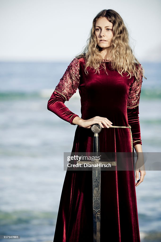 Woman wearing red velvet medieval gown holding a sword