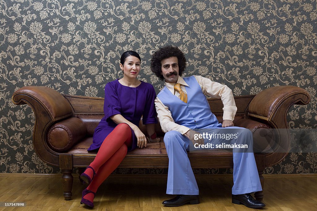 Young couple in 1970s style clothings sitting on leather sofa