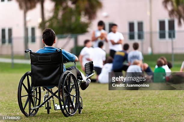 young disabled boy looking upon his peers leaving him out - special needs children stock pictures, royalty-free photos & images