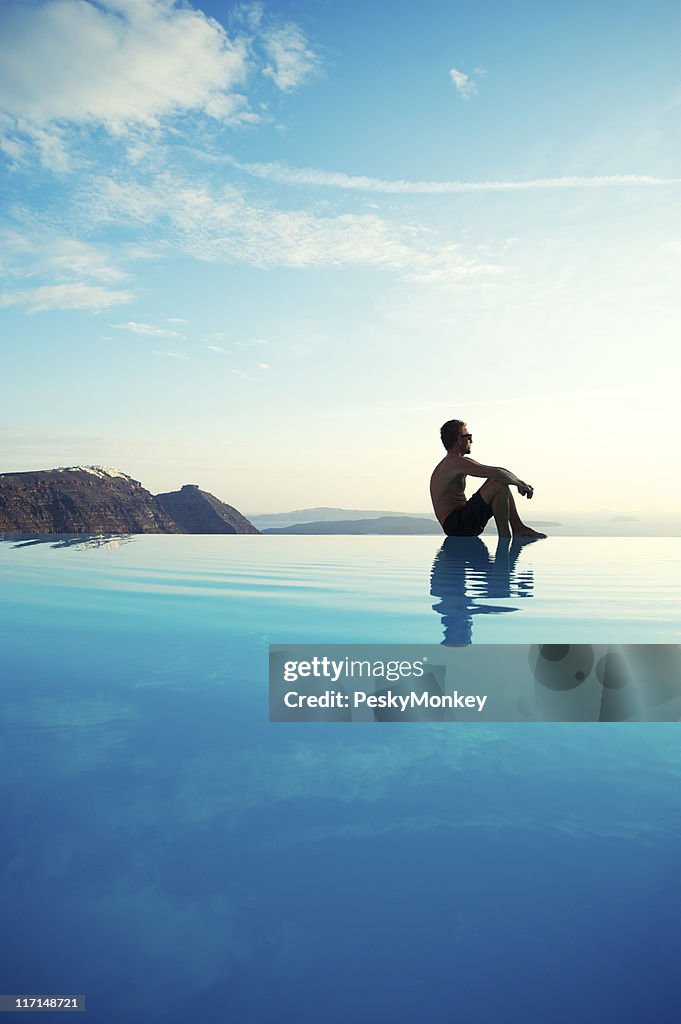 Young Man Sitting Reflecting on Infinity Pool Edge Tourist Resort