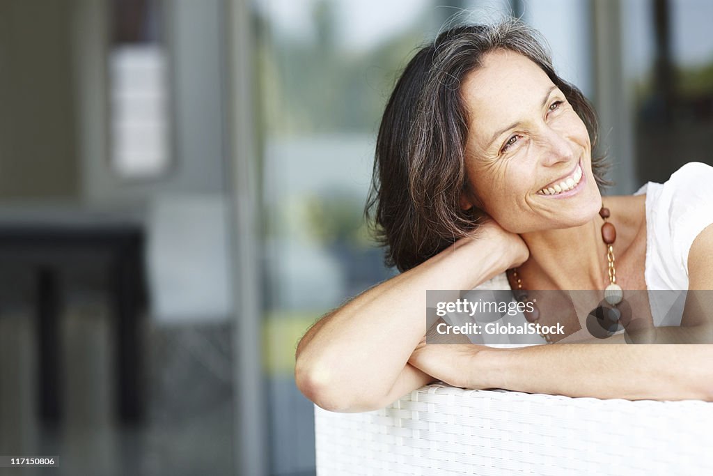 Schöne Reife Frau sitzt auf Sofa lächelnd und Wegsehen