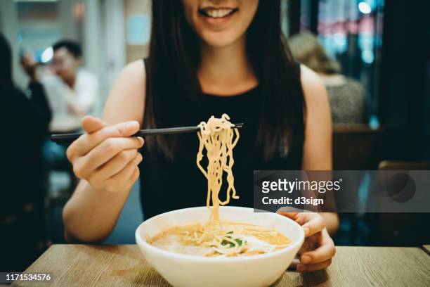 close up shot of smiling young asian woman eating japanese soup noodles in restaurant - ramen noodles stock pictures, royalty-free photos & images