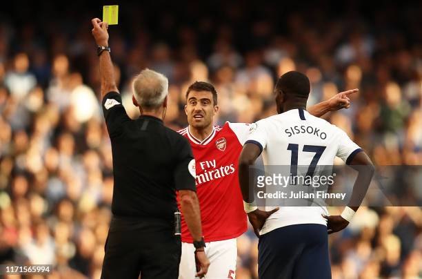 Sokratis of Arsenal is shown a yellow card by referee Martin Atkinson during the Premier League match between Arsenal FC and Tottenham Hotspur at...
