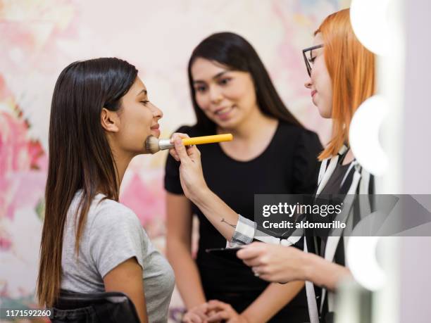 make-up artist putting on make-up to client next to employee - makeup artist stock pictures, royalty-free photos & images