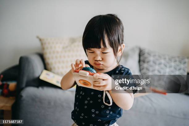 cute little toddler girl making a silly face and looking confused on playing with the toy camera at home - toy camera stock pictures, royalty-free photos & images