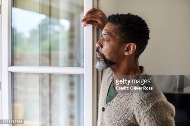 pensive man looking out of window - cuarentena fotografías e imágenes de stock