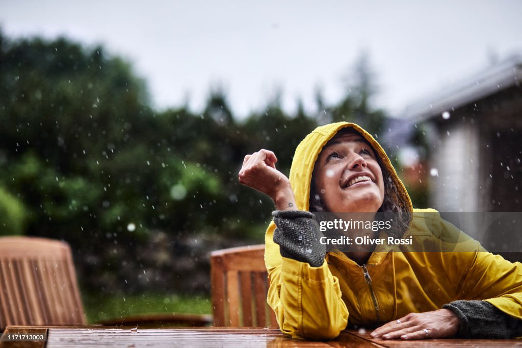 Happy woman wearing raincoat during heavy rain in garden