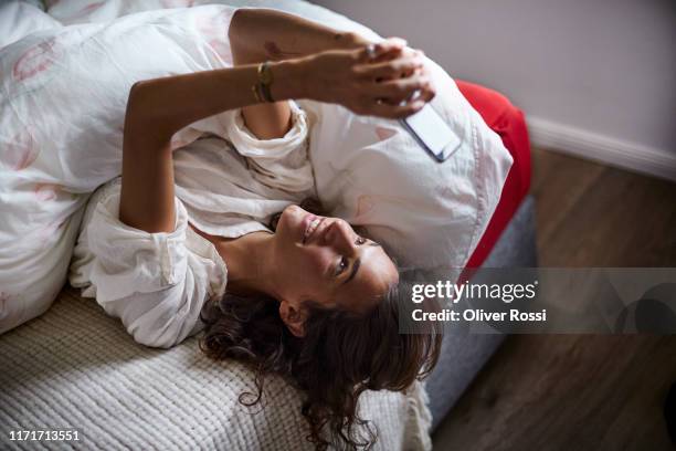 relaxed young woman using cell phone in bed - lazy day fotografías e imágenes de stock