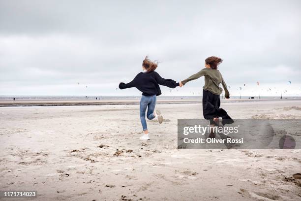happy young woman and girl running on the beach - girl blowing sand stock-fotos und bilder