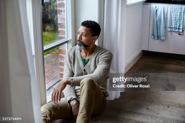 pensive man sitting on the floor looking out of window - 憂鬱 ストックフォトと画像