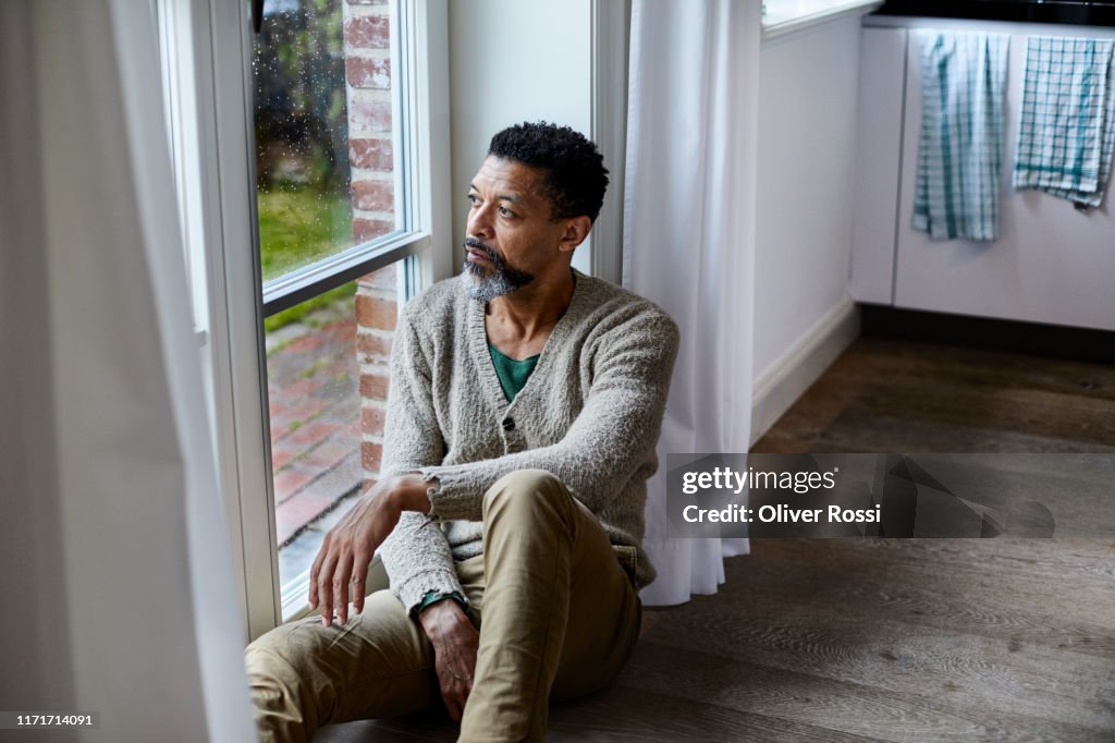 Pensive man sitting on the floor looking out of window