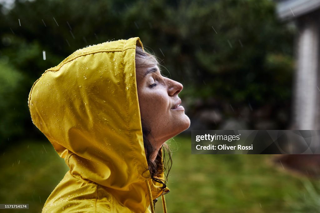 Woman wearing raincoat during heavy rain in garden