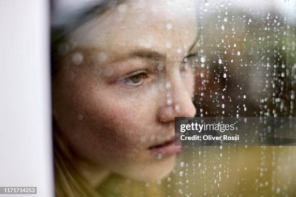 close-up of pensive young woman looking out of window - sad person stock-fotos und bilder