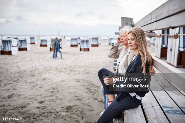 senior woman sitting with her daughter on boardwalk on the beach - mother daughter beach stock pictures, royalty-free photos & images