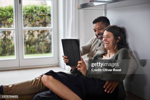 happy mature man and young woman sitting on the floor using tablet - hombre mojado fotografías e imágenes de stock