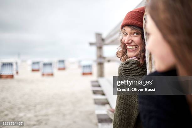 happy young woman looking at girl on boardwalk on the beach - beach shelter ストックフォトと画像