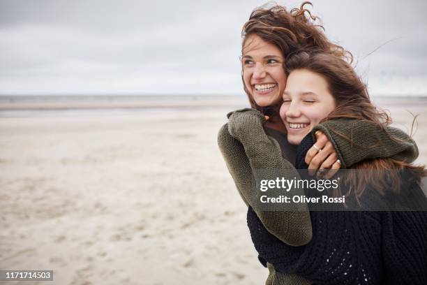 happy young woman hugging girl on the beach - mother and daughter in the wind stock-fotos und bilder